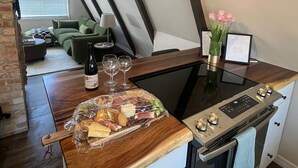 A modern kitchen with a wooden countertop, a built-in oven, and a dining area with a green sofa and a table set with wine glasses and a charcuterie board.