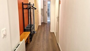 A narrow hallway with wooden flooring, a bench, a radiator, and a clothes rack.