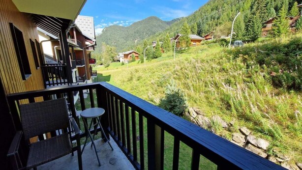 A balcony with wicker furniture and a small table, overlooking a mountainous landscape with houses. - Ski-in/ski-out & foot of the slopes, 3rd floor, view ski slopes, balcony, tv, ski locker, 28m² (Valfréjus)