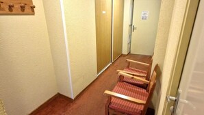 Un couloir doté d’un sol recouvert de moquette, de bancs en bois, d’un porte-manteau et d’une porte sur laquelle est apposée une pancarte.