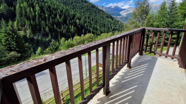 Un balcon offrant une vue sur une chaîne de montagnes boisée et un ciel dégagé.