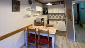 A compact kitchen with white cabinets, a microwave, and a sink. There is a dining area with a table and chairs, and a ceiling light fixture. - Ski-in/ski-out & foot of the slopes, 4th floor, balcony, tv, ski locker, 40m², Valfréjus (Valfréjus)