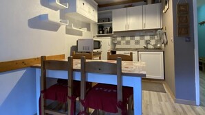 A compact kitchen with white cabinets, a wooden dining table with red chairs, and a clock on the wall. - Ski-in/ski-out & foot of the slopes, 4th floor, balcony, tv, ski locker, 40m², Valfréjus (Valfréjus)
