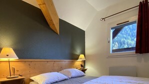 A bedroom with a bed, two bedside lamps, a window with a view of trees, and a wooden ceiling beam. - Ski-in/ski-out & foot of the slopes, 4th floor, balcony, tv, ski locker, 40m², Valfréjus (Valfréjus)