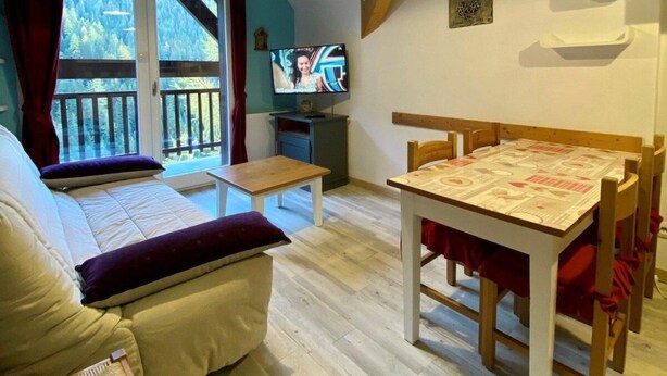A cozy room with a bed, a wooden table, a TV, and a balcony with a view of trees. - Ski-in/ski-out & foot of the slopes, 4th floor, balcony, tv, ski locker, 40m², Valfréjus (Valfréjus)
