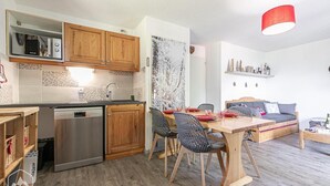 A compact kitchen with wooden cabinets, a built-in microwave, and a dishwasher. There is a dining area with a wooden table and chairs, and a sofa in the living space. - 100m from ski slopes, Ground floor, terrace, ski locker, 40m², Valfréjus (Valfréjus)
