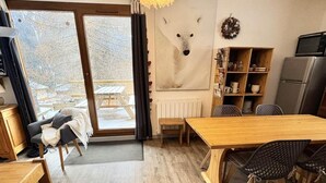 A modern interior with a wooden dining table, chairs, a sofa, and a large window with a view of a snowy landscape. - 100m from ski slopes, Ground floor, terrace, ski locker, 40m², Valfréjus (Valfréjus)