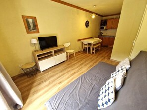 A compact room with a bed, a TV, a small dining table, and a kitchenette.