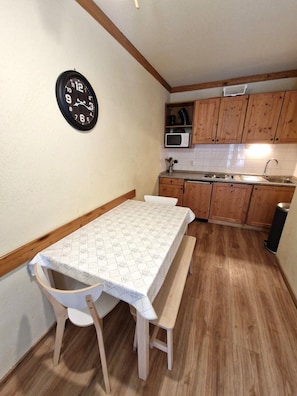 A small kitchen with wooden cabinets, a microwave, and a clock on the wall.