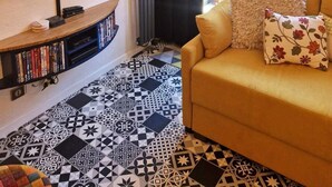 A living room with a TV mounted on the wall, a sofa with floral cushions, and a patterned floor. - 30m from ski slopes, 4th floor, balcony, tv, ski locker, 19m², Valfréjus (Valfréjus)
