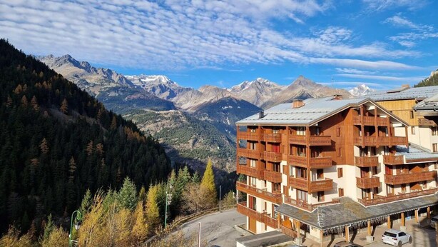 A multi-story building with balconies, set against a mountainous backdrop. - Resort center, 4th floor, view open, balcony, ski locker, 19m², Valfréjus (Valfréjus)