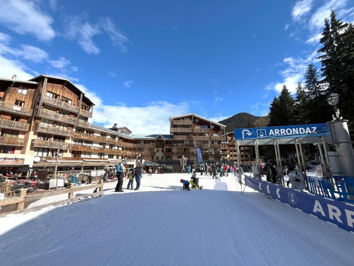 A ski resort with a large snow-covered area, a sign for 'Arrondaz', and multi-story buildings with balconies.