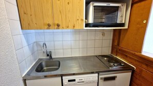 A compact kitchen with wooden cabinets, a built-in microwave, a stainless steel sink, and a dishwasher. - Resort center, 4th floor, view open, balcony, ski locker, 19m², Valfréjus (Valfréjus)
