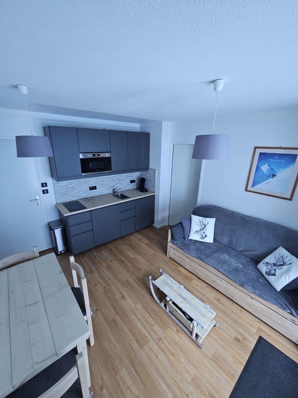 A compact living space with a kitchenette, a sofa with decorative pillows, a small dining table, and a pull-out chair.