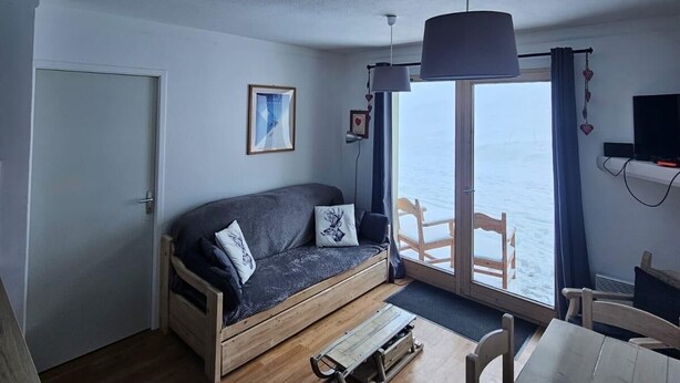 Quarto aconchegante com sofá, uma mesa pequena e vista para o mar através de uma janela grande.