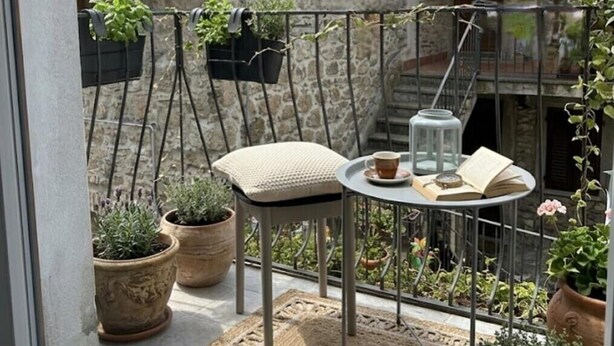 A balcony with a small table, two chairs, potted plants, and a view of old stone buildings. - WelcHome Vitorchiano double room with balcony  (Vitorchiano)