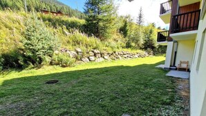 A well-maintained grassy yard with a stone wall and a building with a balcony. - Ski-in/ski-out & foot of the slopes, Ground floor, view mountain, terrace, balcony, tv, ski locker (Valfréjus)