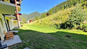 A residential area with a well-maintained lawn, a wooden bench, and a building with balconies. - Ski-in/ski-out & foot of the slopes, Ground floor, view mountain, terrace, balcony, tv, ski locker (Valfréjus)
