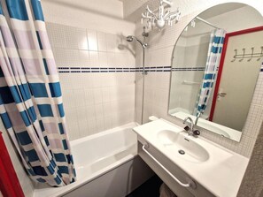 A bathroom with a white bathtub, a sink with a mirror, and a shower area.