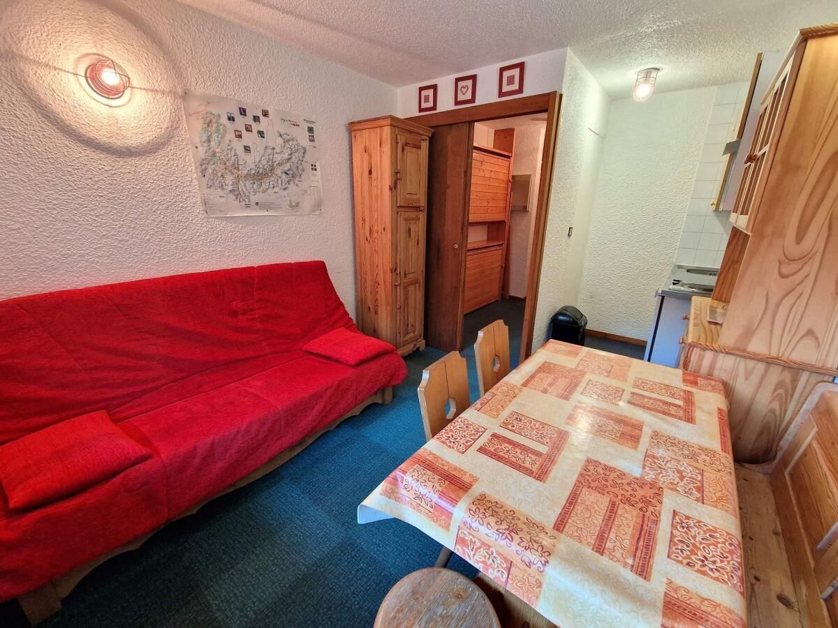 Una habitació amb un sofà vermell, una taula de dinar de fusta amb un mantell estampat i un armari de fusta.