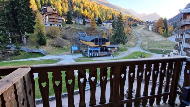 Una località montana con ringhiera in legno sul balcone, una seggiovia e edifici con balconi affacciati sulla valle.