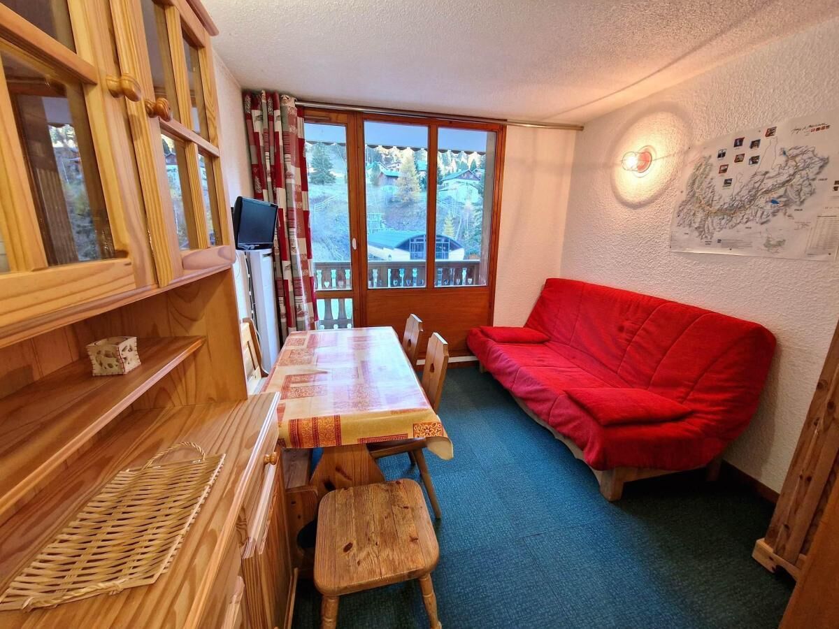 A cozy room with a wooden table, a red sofa, and a large window with a view of a snowy landscape.