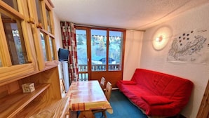 Una stanza accogliente con un tavolo in legno, un divano rosso e un'ampia finestra che si affaccia su un paesaggio innevato.