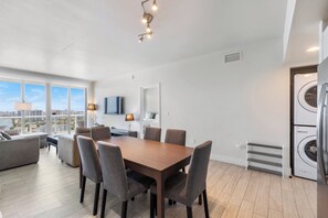 A modern living room with a dining table, comfortable seating, a flat-screen TV, and a large window offering a city view. - ★★★★★ Intracoastal Dream Stay / Stylish 2BR with Spectacular Sky Views (Hallandale Beach)