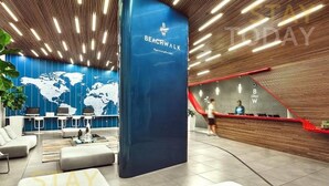 Un moderno vestíbulo de hotel con un mostrador de recepción azul, un mapa mundial en la pared y una escalera que conduce al piso superior.
