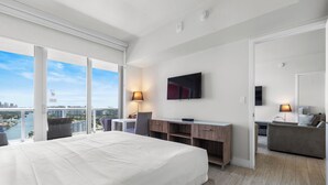 Una habitación de hotel moderna con una cama grande, un escritorio, un televisor y un balcón con vista a la ciudad.