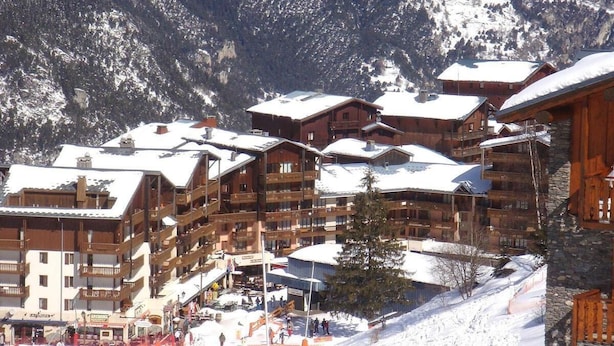 Una stazione sciistica con edifici in legno a più piani, piste da sci e montagne sullo sfondo.