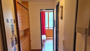 Un couloir étroit doté d’un plancher en bois, d’un radiateur et d’une porte donnant sur une pièce avec une fenêtre et un rideau rouge.