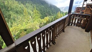 Un balcon doté d’une balustrade en bois, donnant sur une zone montagneuse couverte de forêts.