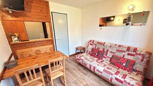 Un espace de vie compact comprenant une table et des chaises en bois, un canapé à motifs et un téléviseur fixé au mur.