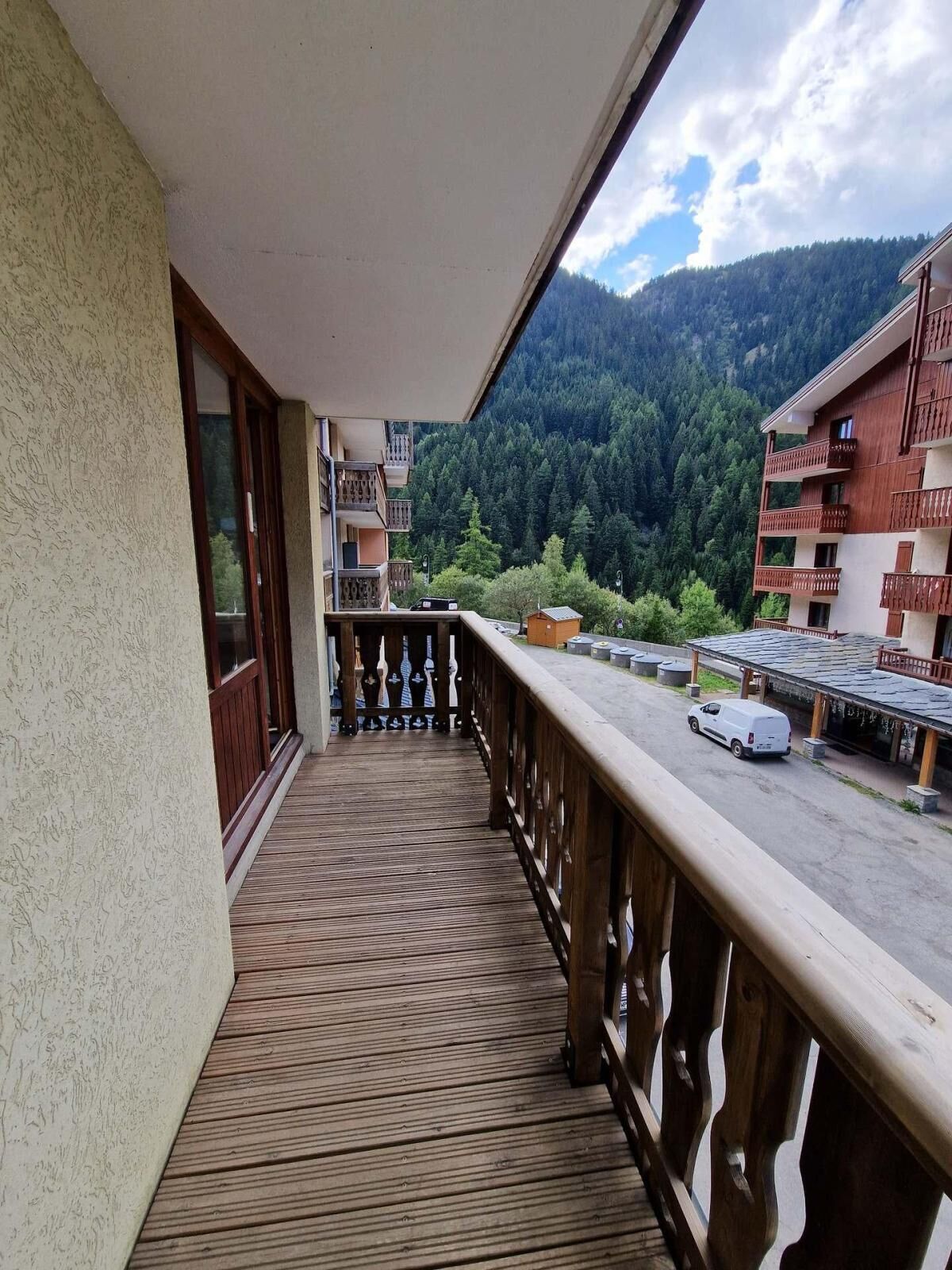Un balcón de madera con vista a una montaña boscosa y un estacionamiento.
