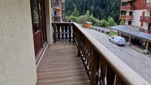 Un balcón de madera con vista a una montaña boscosa y un estacionamiento.