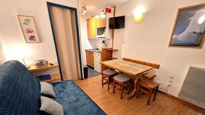 Un espacio habitable compacto con sofá, una mesa de comedor con sillas, una kitchenette y un televisor montado en la pared.