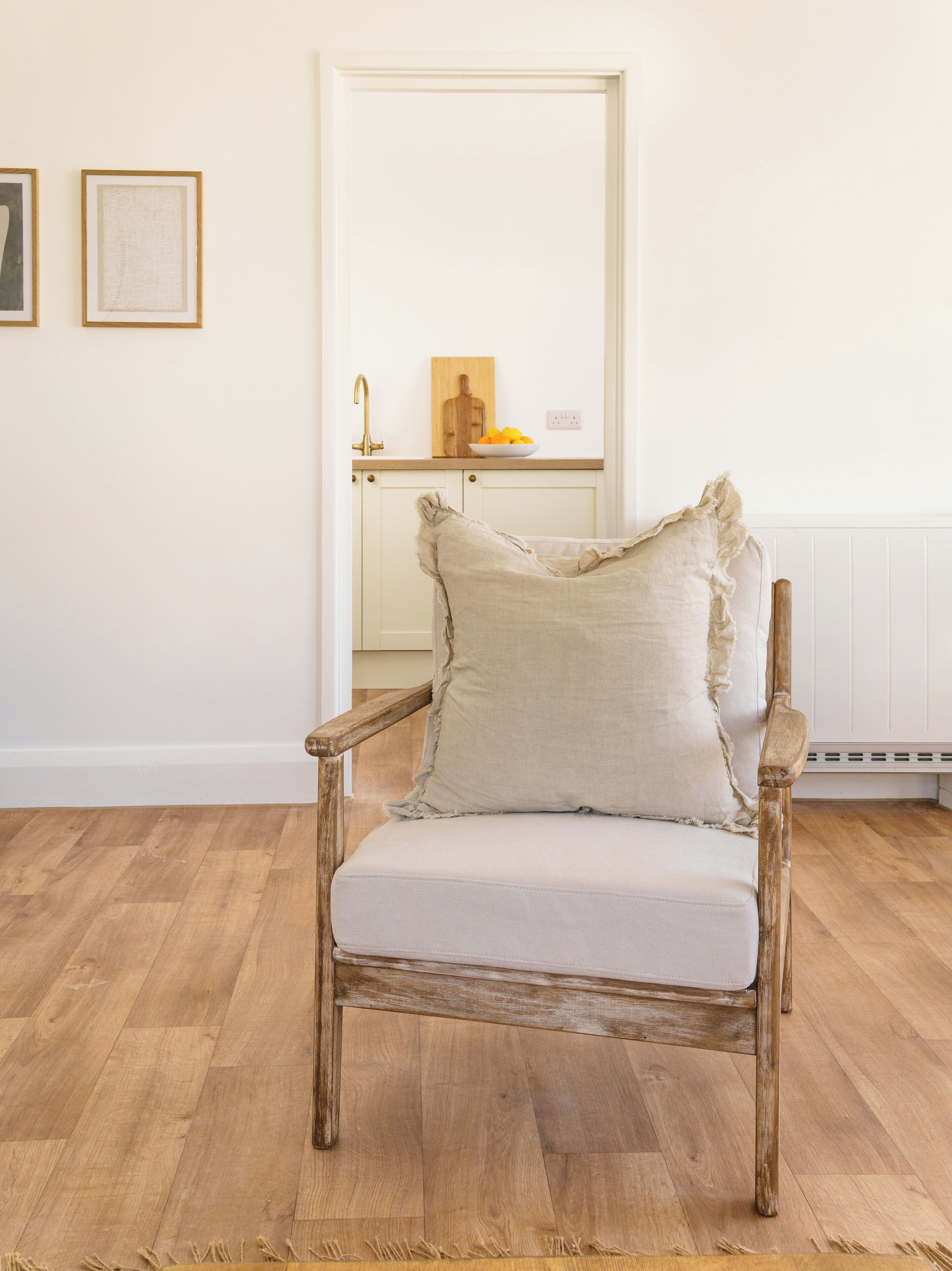 A rustic wooden chair with a distressed finish and a light-colored cushion, positioned in a room with wooden flooring and white walls.