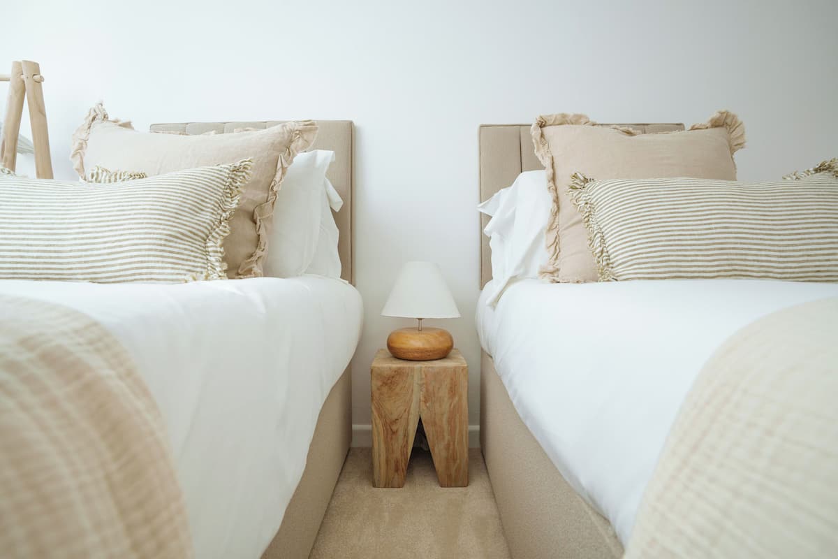 A bedroom with two beds, each with a ruffled headboard, a wooden nightstand with a lamp, and a beige carpet.