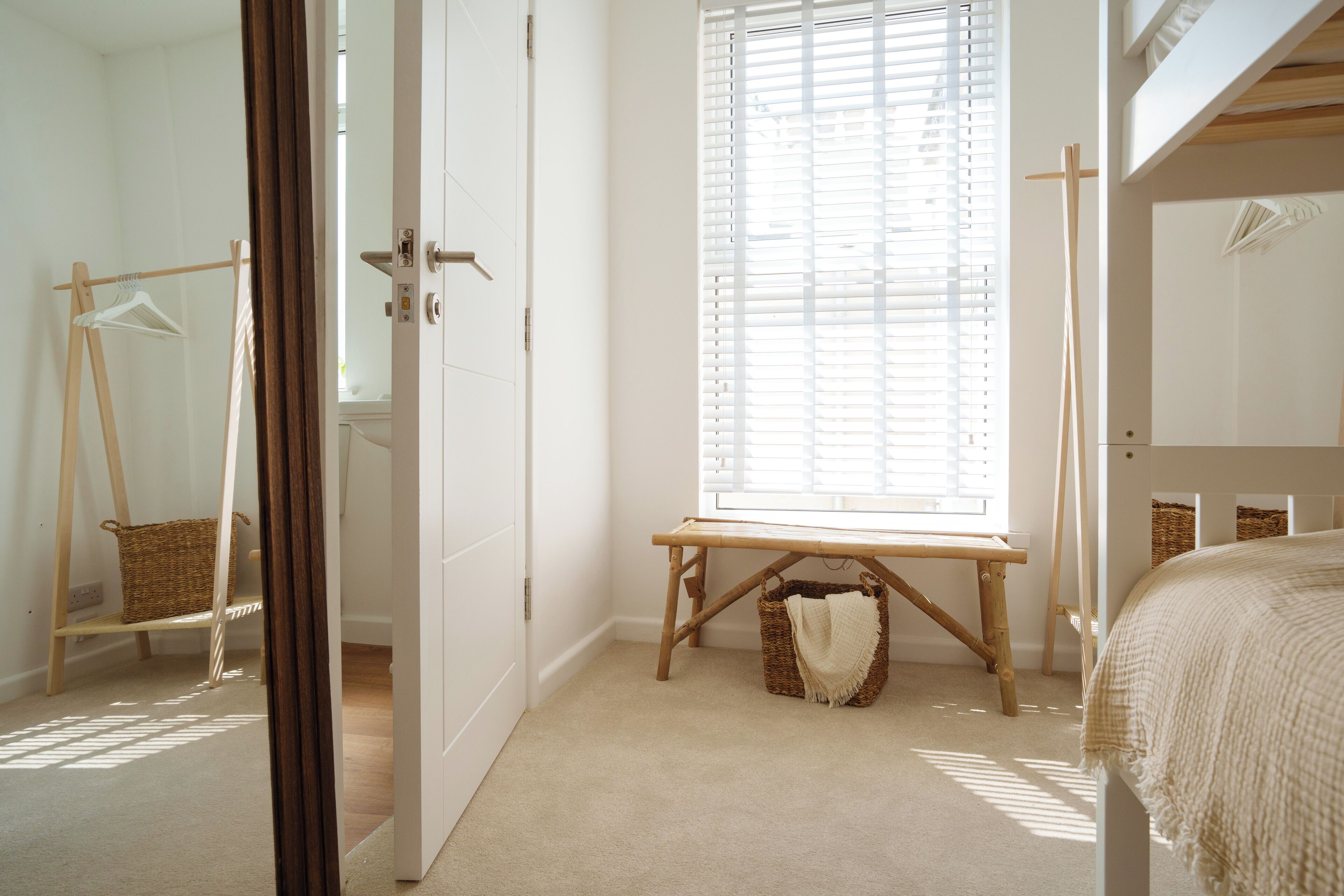 A bedroom with a bed, a window with blinds, a wooden bench, and a wardrobe.