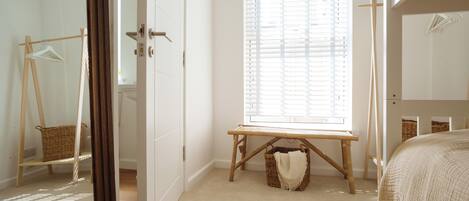A bedroom with a bed, a window with blinds, a wooden bench, and a wardrobe.