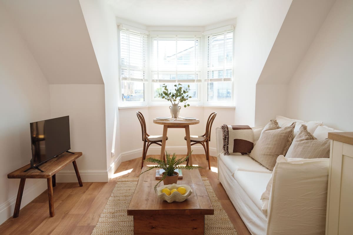 A cozy living room with a wooden coffee table, a white sofa, and a TV on a stand.