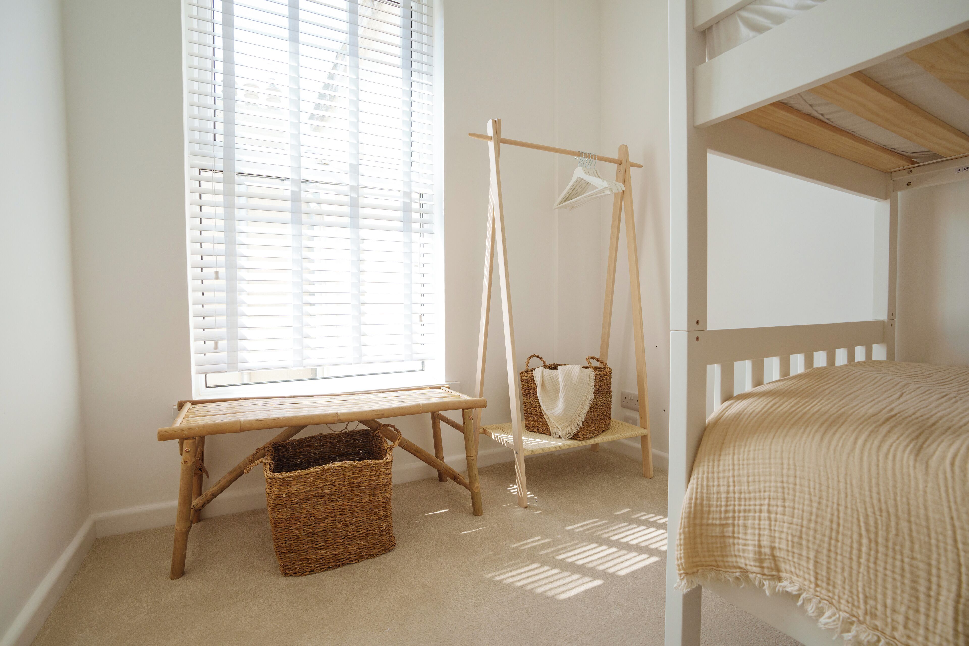 Una habitación con ventana, cama, columpio de madera y una cesta.
