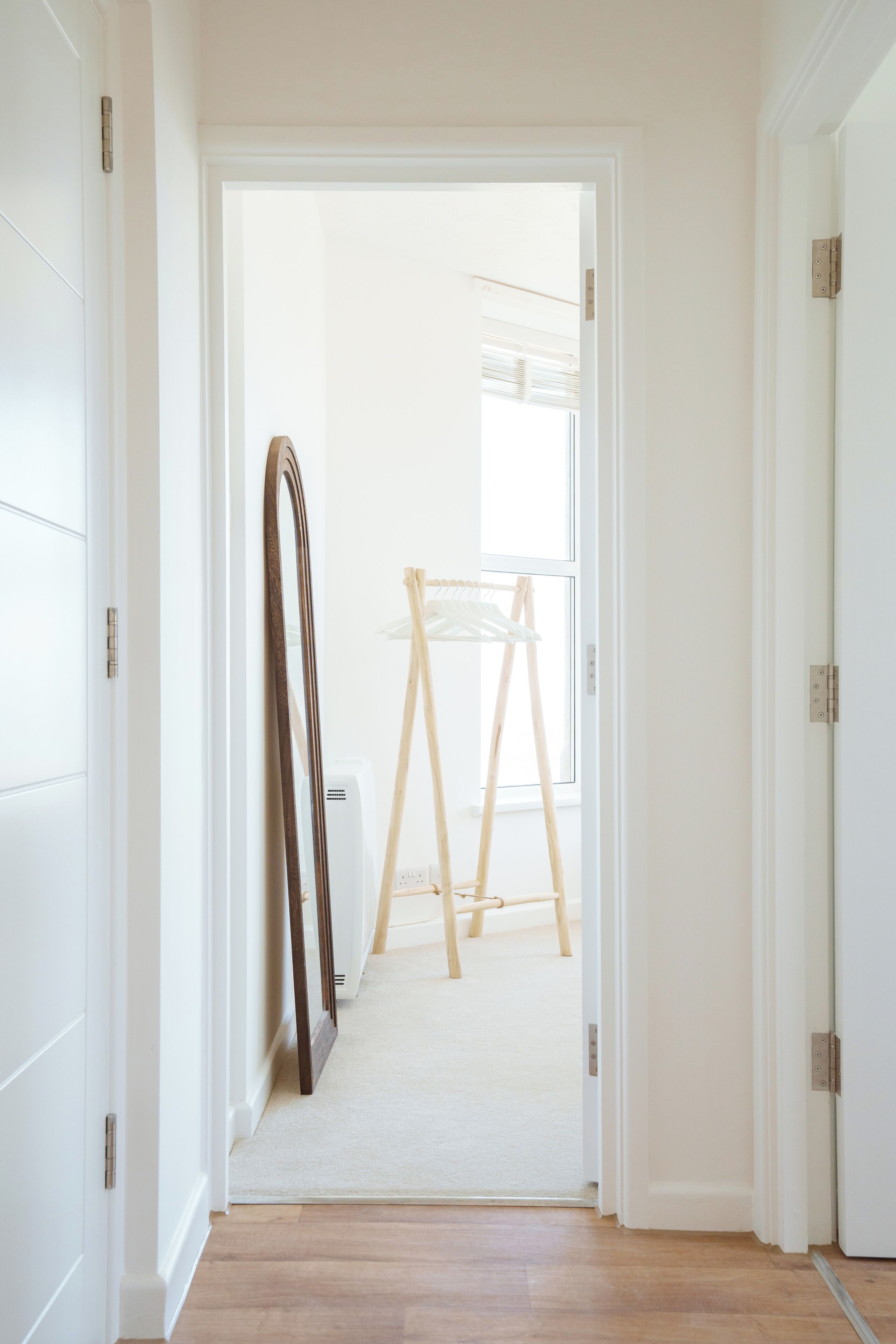 Een gang met een houten vloer, een witte deurkozijn en een witte deur.