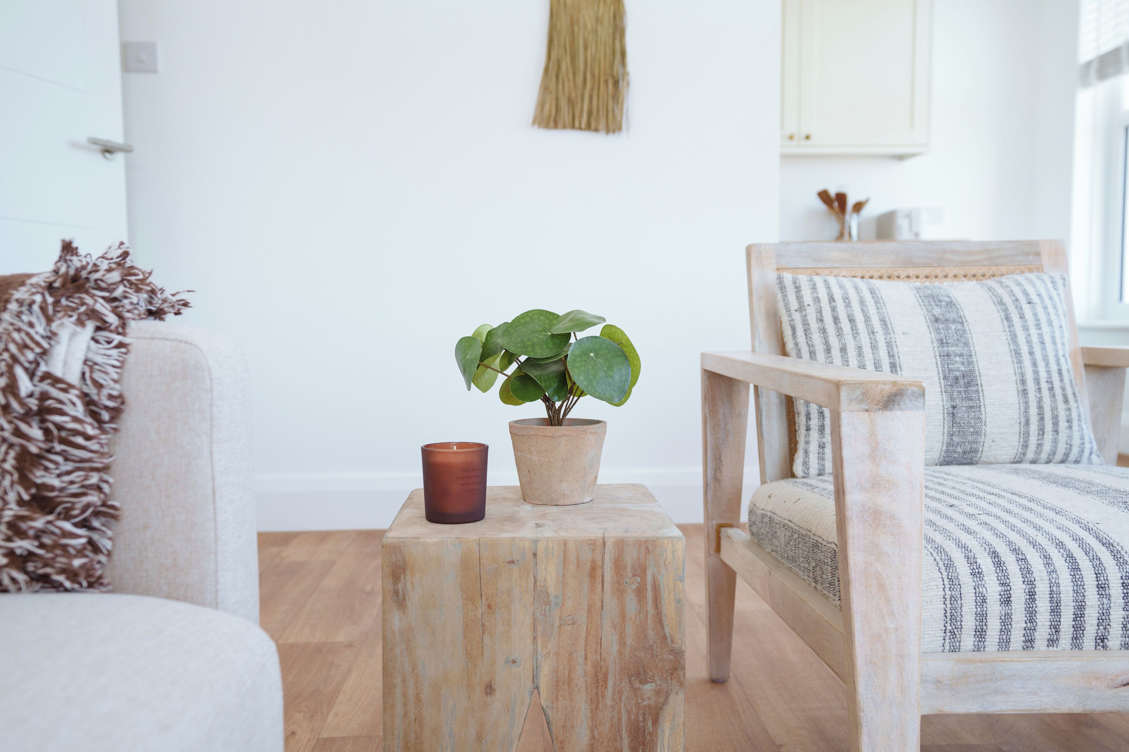 Una sala acogedora con un taburete de madera, una planta en maceta y una vela.