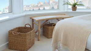 A bedroom with a large window, a bed, two wicker baskets, a small wooden table, and a potted plant. - VESTO  Coastal Hideout (Newquay)