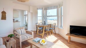 A spacious living room with a wooden dining table, chairs, a sofa, and a TV. - VESTO  Coastal Hideout (Newquay)