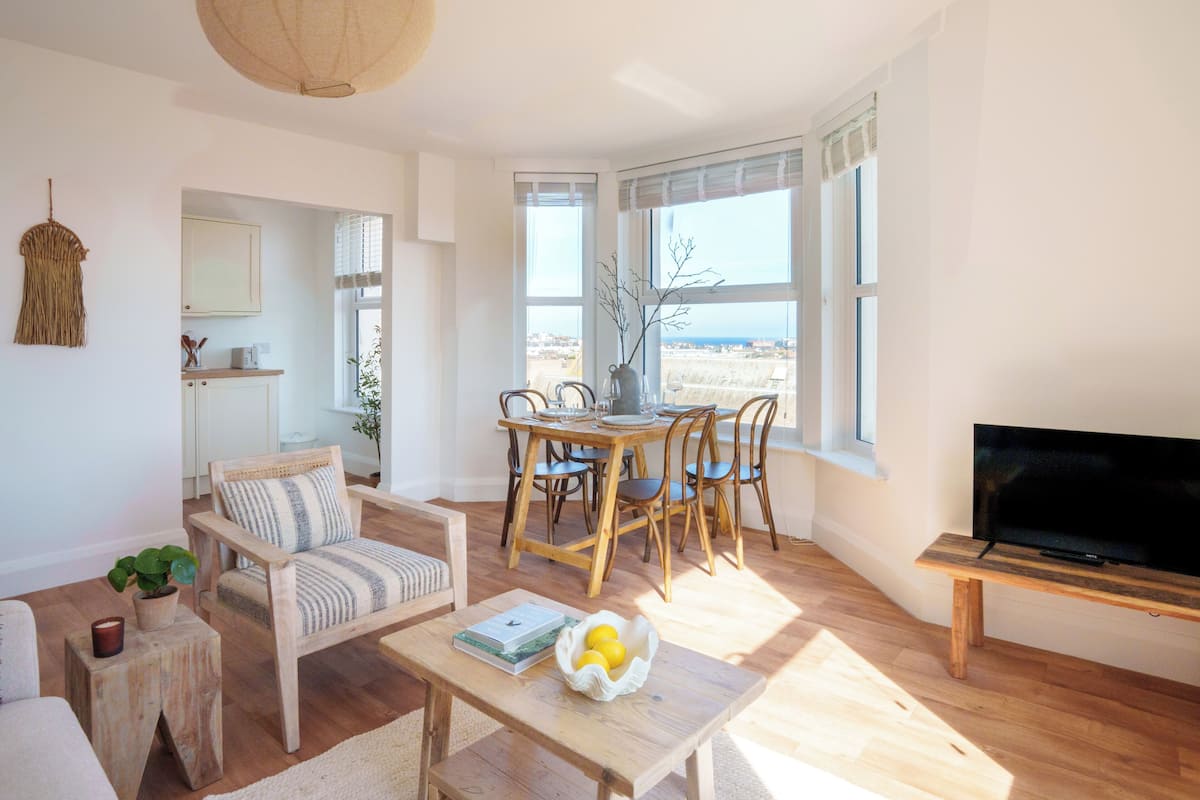 A spacious living room with a wooden dining table, chairs, a sofa, and a TV.