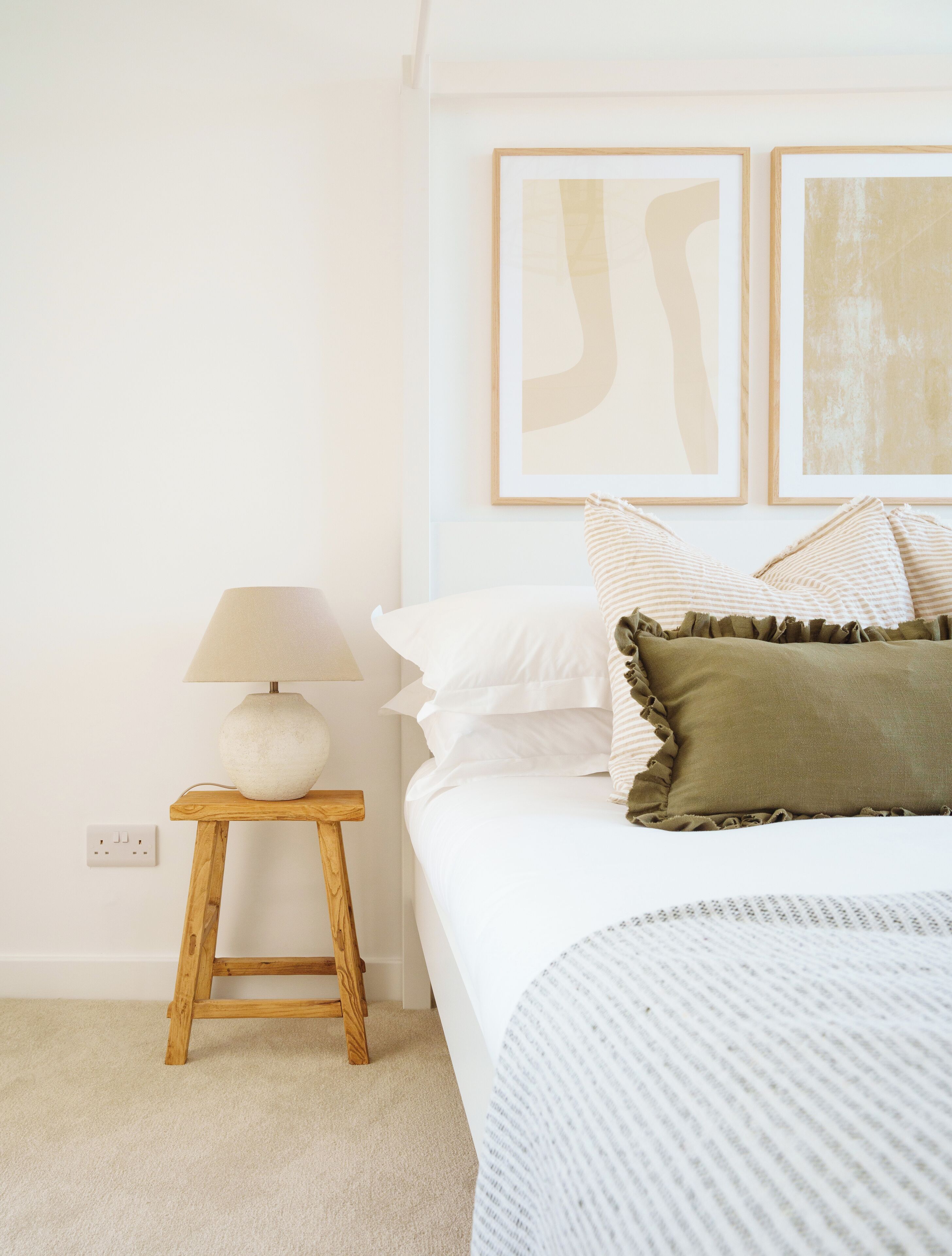 A bedroom with a bed, a nightstand with a lamp, and two framed abstract paintings on the wall.