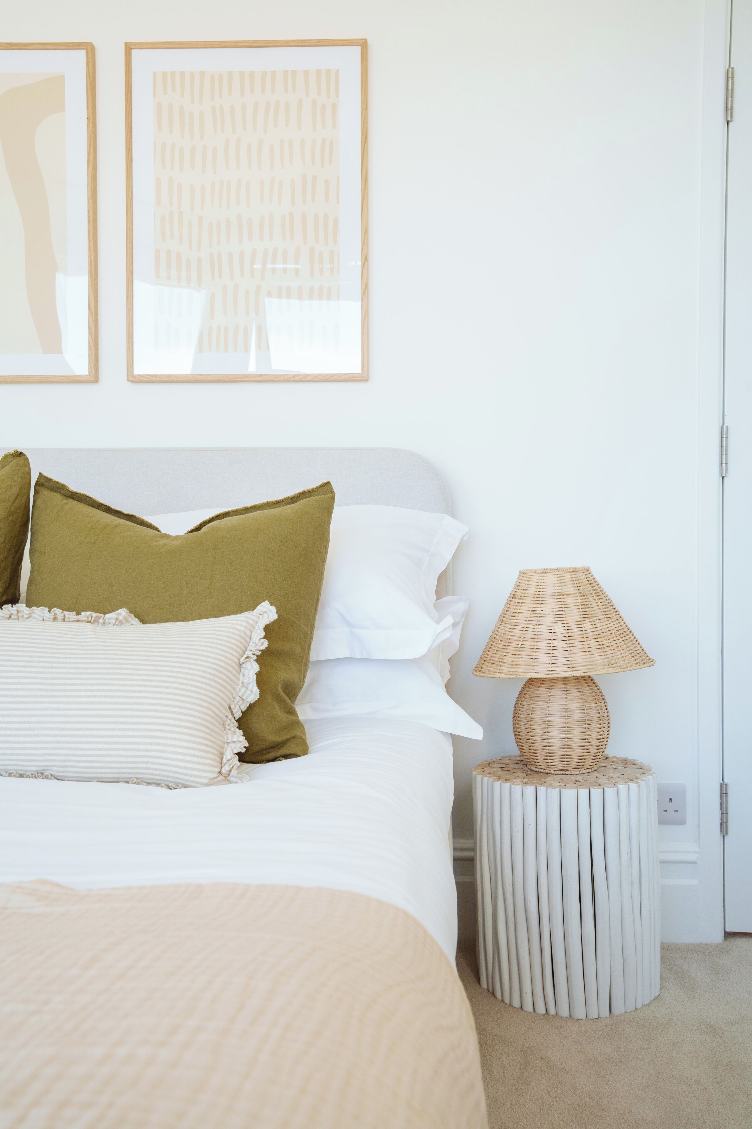 Un dormitorio ordenado con cama, almohadas, una lámpara de noche y cuadros en la pared.